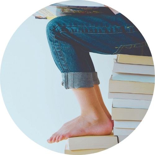 Donna in jeans a piedi scalzi legge seduta su una pila di libri